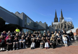 Uczniowie siedzących na schodach przed Museum Ludwig, czyli Muzeum Sztuki. W tle, po prawej stronie, wznosi się imponująca Katedra Kolońska.