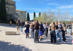 Uczniowie biorący udział w edukacyjnej podróży do Francji na tle malowniczego, kamiennego budynku w stylu śródziemnomorskim.