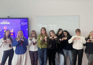 Grupa uczestniczek warsztatów stojących w sali dydaktycznej przed tablicą oraz ekranem multimedialnym