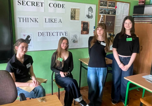 Uczniowie prezentują przygotowaną scenę detektywistyczną, stojąc na tle planszy z hasłem „Secret code – think like a detective”, wprowadzając uczestników w klimat wydarzenia.