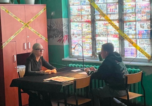 Uczestnik gry detektywistycznej prowadzi przesłuchanie przy specjalnie zaaranżowanym stanowisku, analizując dokumenty i zbierając informacje w scenografii inspirowanej światem Sherlocka Holmesa.