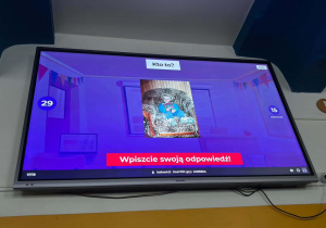 Na ekranie wyświetlono pytanie quizowe z archiwalnym zdjęciem dziecka, które uczestnicy próbują dopasować do właściwego nauczyciela, wpisując swoje odpowiedzi w aplikacji Kahoot.