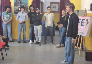 Uczestnik warsztatów prezentuje temat przed grupą stojącą w szkolnej sali podczas spotkania programu Erasmus in Schools.
