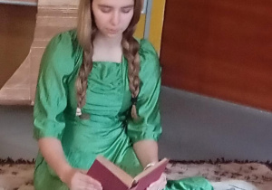 Osoba w zielonym stroju siedzi na dywanie i czyta książkę w scenie inspirowanej twórczością Jane Austen